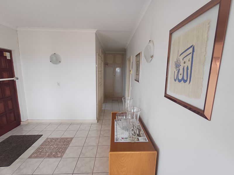 A bright entrance hallway featuring tiled flooring, built-in storage cupboards, and wall-mounted lighting, leading towards the interior living spaces.