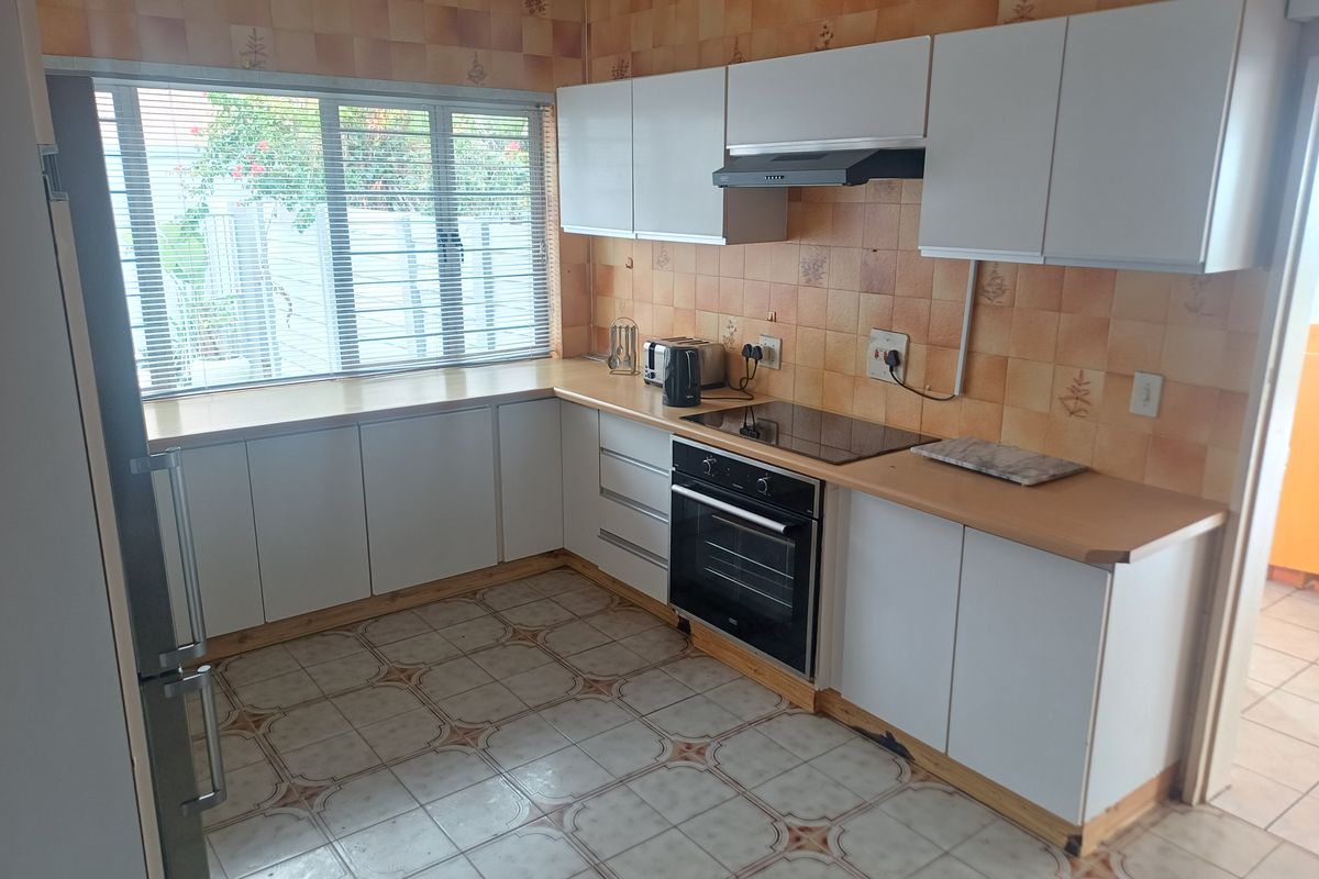 A functional kitchen featuring white cabinetry, laminate countertops, built-in oven and hob, and a tiled backsplash.