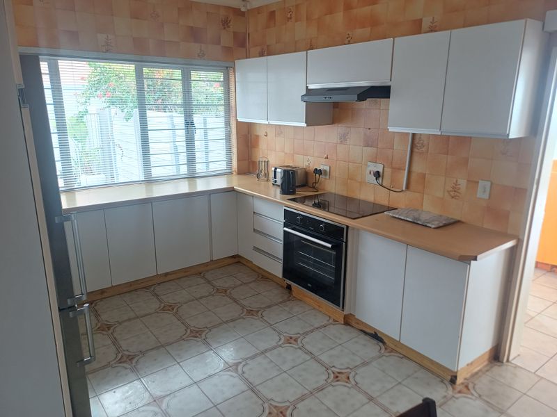 A functional kitchen featuring white cabinetry, laminate countertops, built-in oven and hob, and a tiled backsplash.