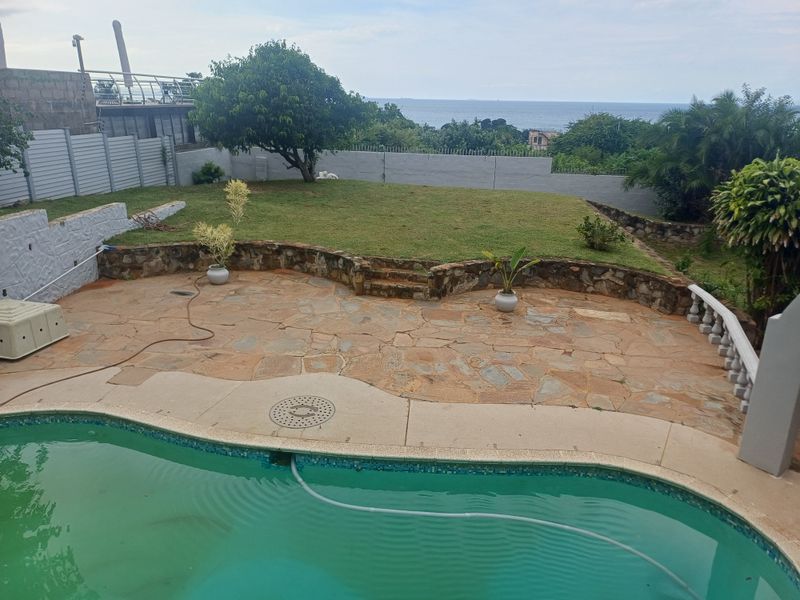 Outdoor pool area featuring a stone-paved patio, retaining wall, and perimeter fencing with ocean views.