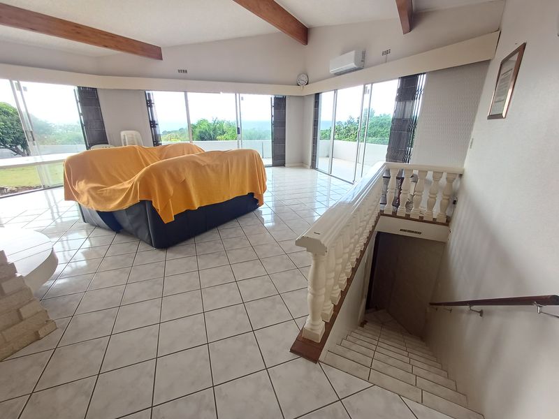 Spacious living area featuring exposed timber beams, tiled flooring, and large sliding glass doors leading to an outdoor space, with an internal staircase.