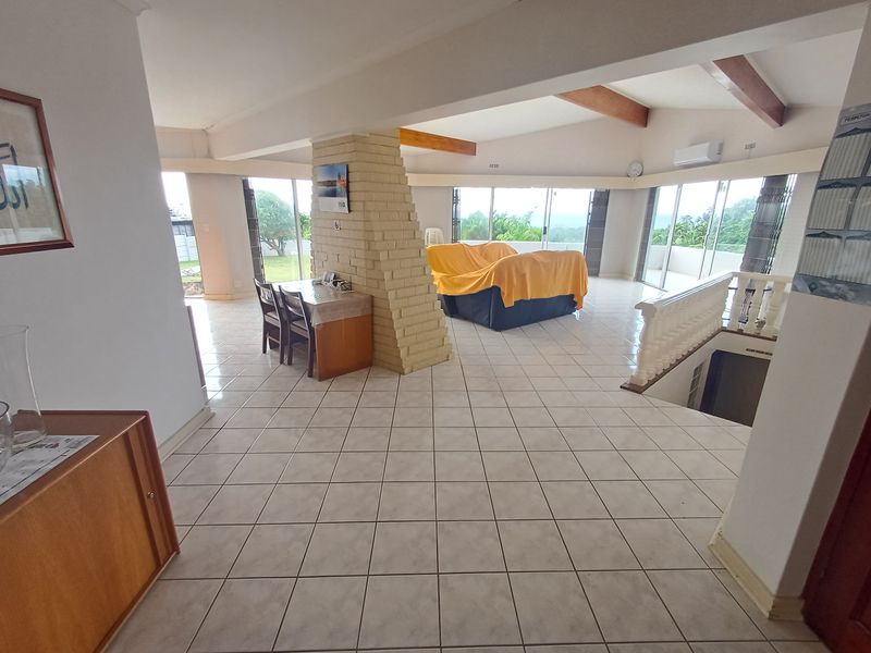 Spacious open-plan living area featuring exposed timber beams, a central brick column, ceramic tile flooring, and large sliding doors leading to the exterior.
