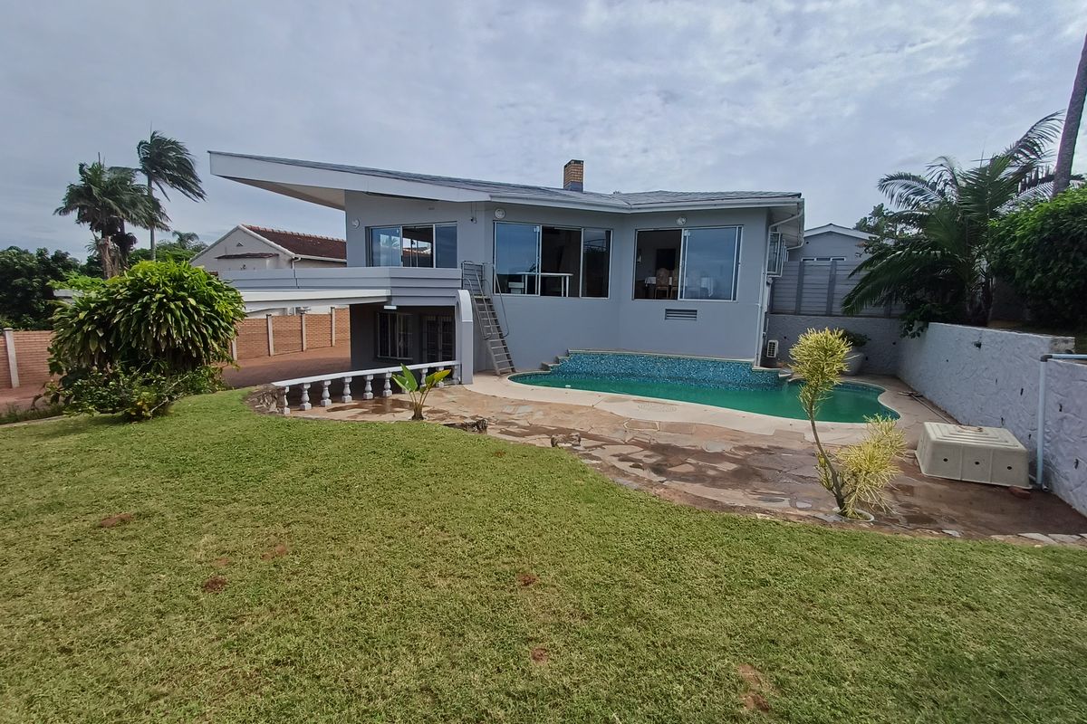Rear exterior view of the house featuring a swimming pool, paved patio area, and a spacious lawn with boundary walling.