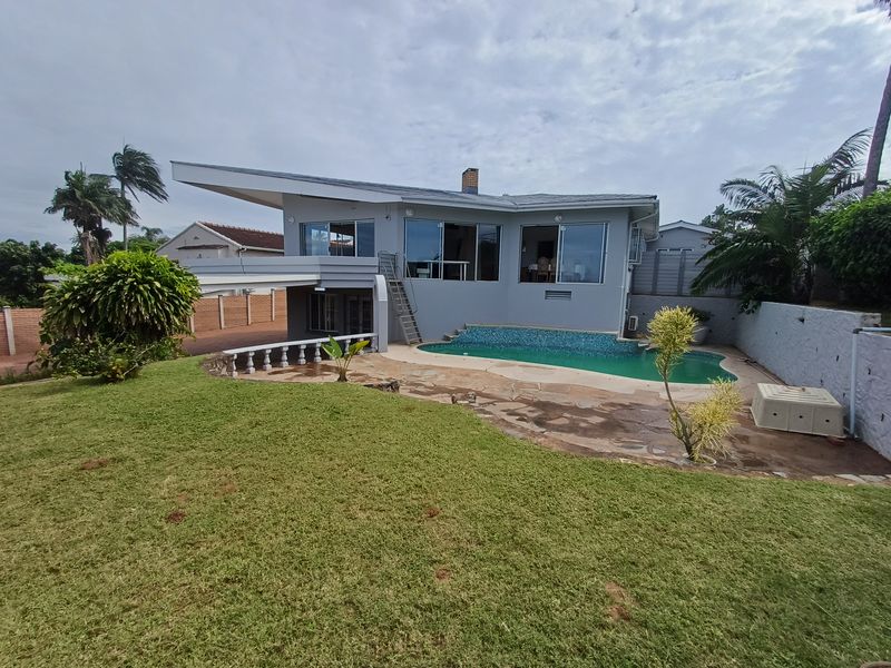 Rear exterior view of the house featuring a swimming pool, paved patio area, and a spacious lawn with boundary walling.