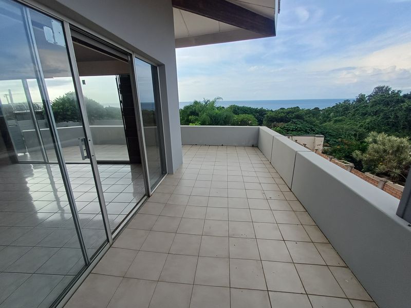 Spacious covered balcony featuring tiled flooring, sliding glass doors, and expansive views of the surrounding landscape and ocean.