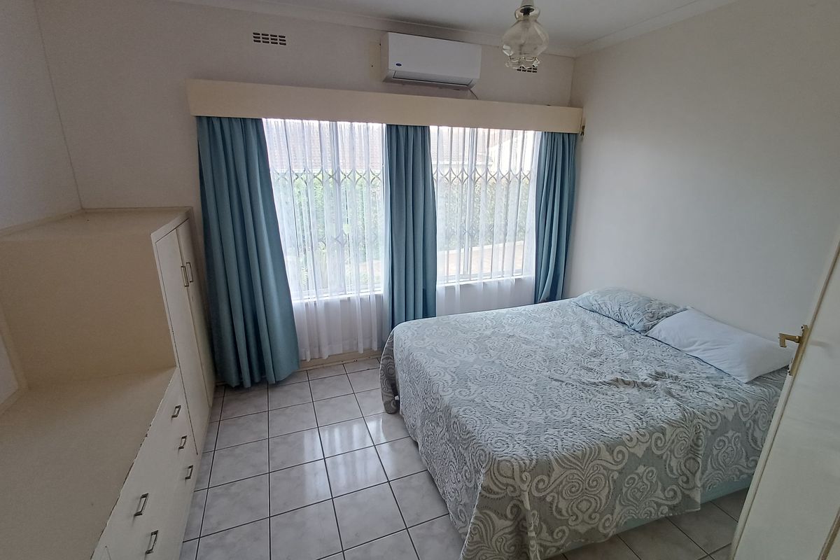 A functional bedroom featuring tiled flooring, built-in cupboards, and a wall-mounted air conditioning unit, providing a comfortable and practical living space.