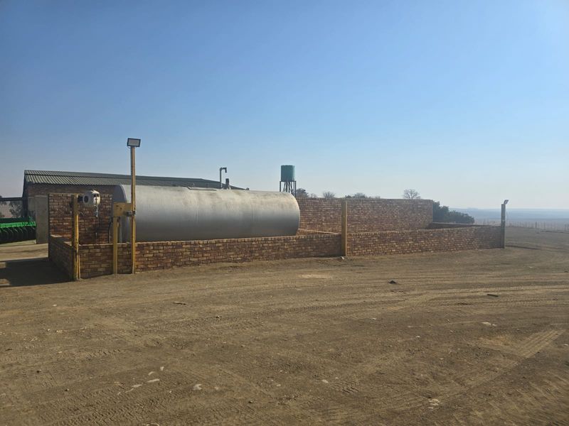 A functional farm utility area featuring a large fuel storage tank enclosed within a brick containment wall and an elevated water tank.