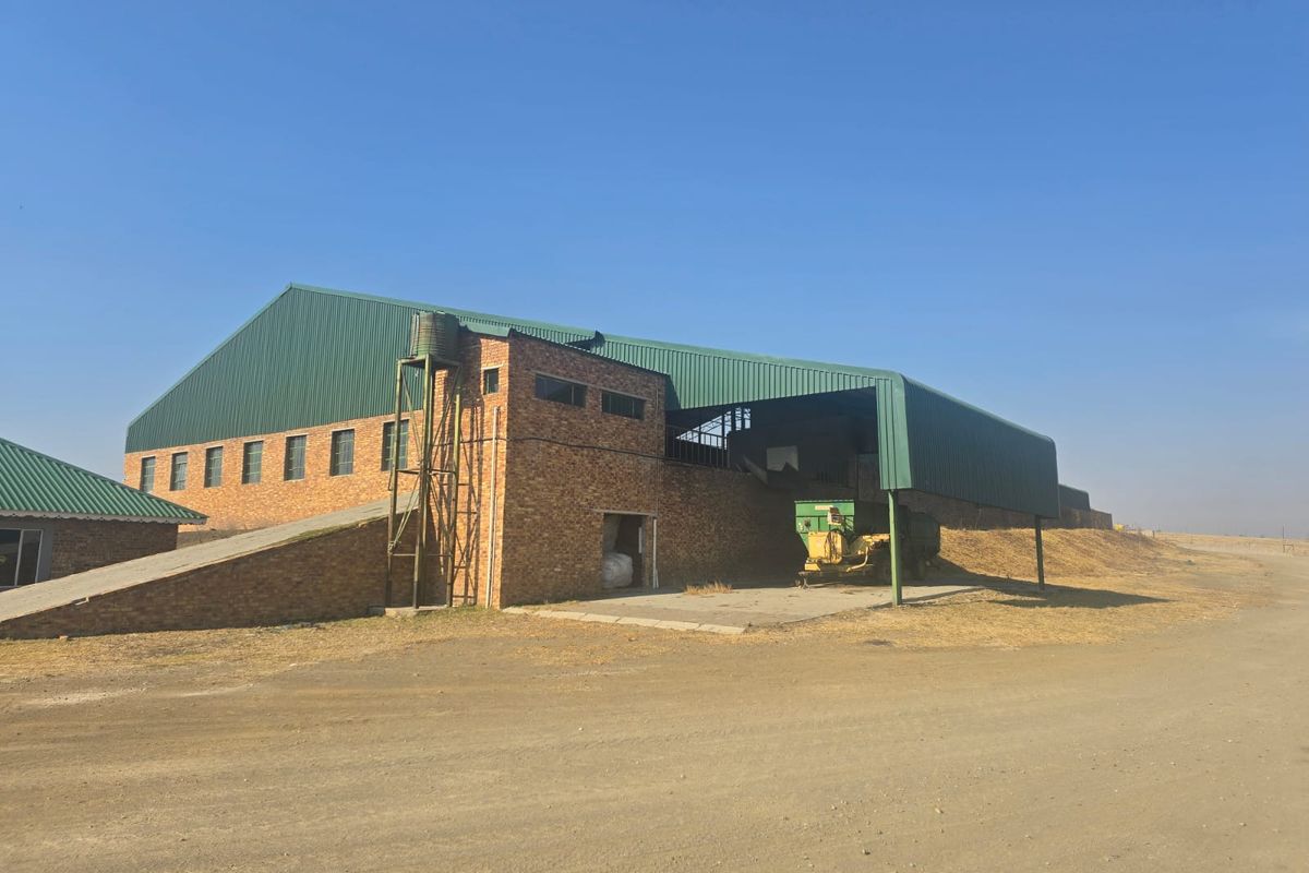 Large agricultural barn featuring face brick construction, a green corrugated metal roof, and an integrated concrete ramp for farm operations.