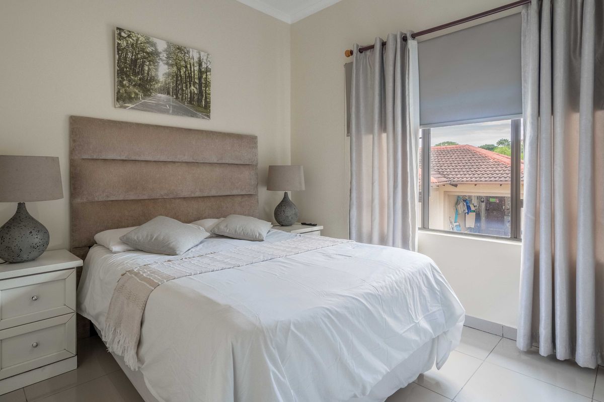 A well-maintained bedroom featuring neutral wall tones, tiled flooring, and a large window with integrated blinds and curtain fixtures.