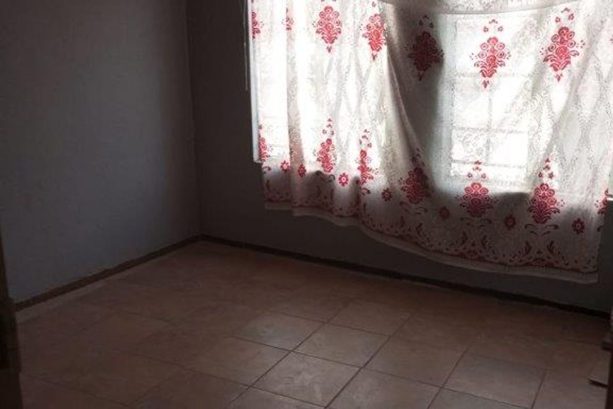 An empty bedroom featuring tiled flooring and a window with existing curtain fixtures.