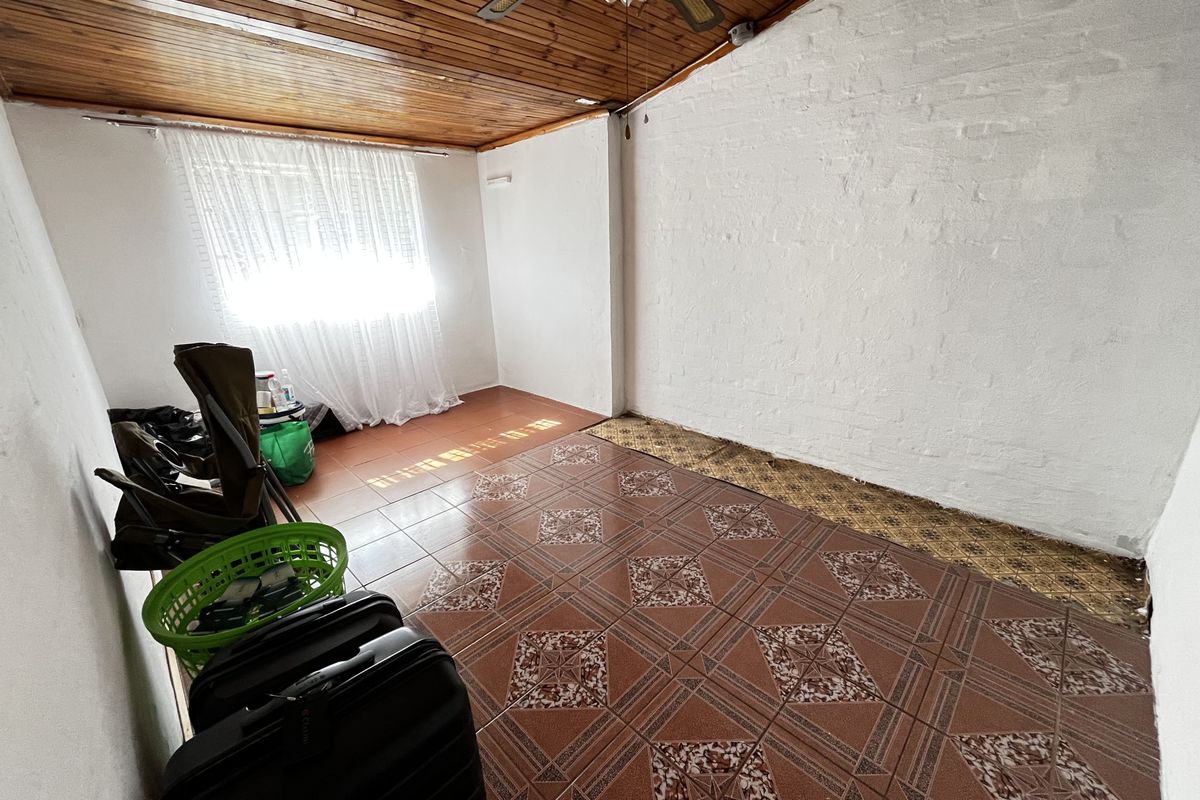 An empty living area featuring a timber-clad ceiling, ceiling fan, and patterned ceramic floor tiles with a painted brick feature wall.