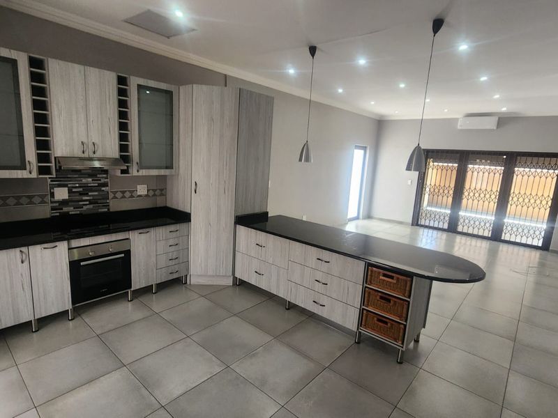 Spacious open-plan kitchen and living area featuring modern light-wood cabinetry, granite countertops, integrated appliances, and large tiled floors leading to a secure patio.