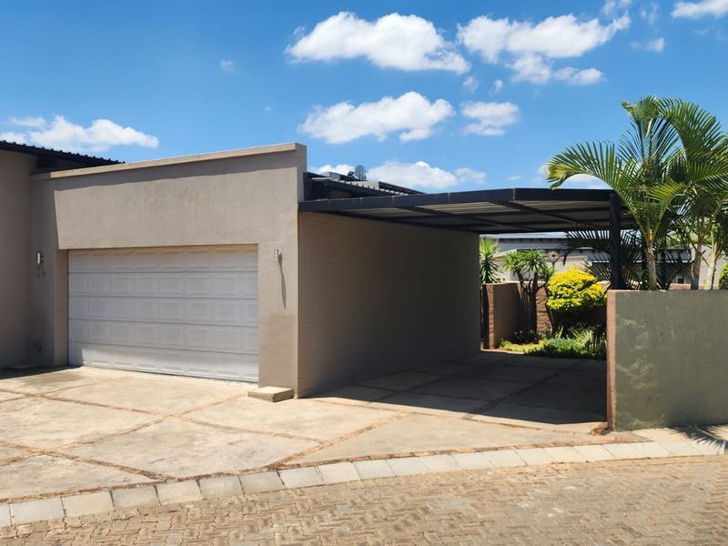 Front exterior view featuring a double garage, attached carport, and paved driveway with a boundary wall.