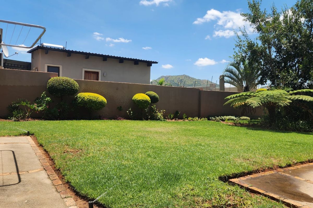 A well-maintained rear garden featuring a manicured lawn, paved pathways, and a solid boundary wall with established landscaping.