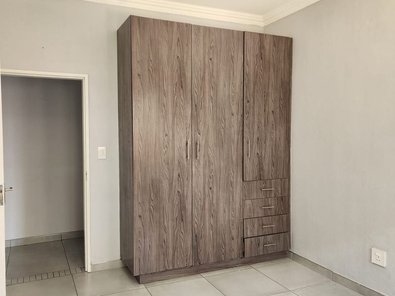 A clean, empty bedroom featuring modern wood-grain built-in cupboards, neutral tiled flooring, and simple wall finishes.