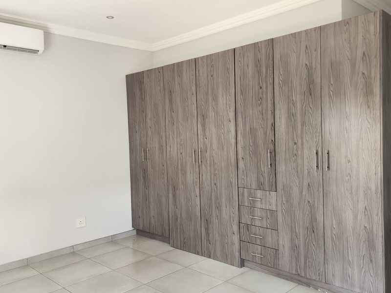 Spacious bedroom featuring extensive built-in wooden cabinetry, neutral tiled flooring, and a wall-mounted air conditioning unit.