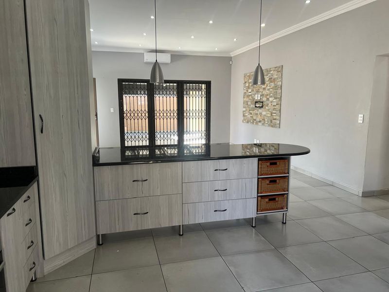 Modern kitchen featuring a central island with granite countertops, light wood-grain cabinetry, tiled flooring, and a decorative stone feature wall.