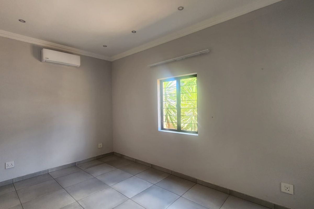 A clean, empty bedroom featuring neutral tiled flooring, recessed lighting, and a wall-mounted air conditioning unit.