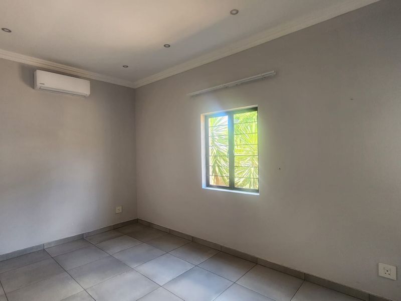A clean, empty bedroom featuring neutral tiled flooring, recessed lighting, and a wall-mounted air conditioning unit.