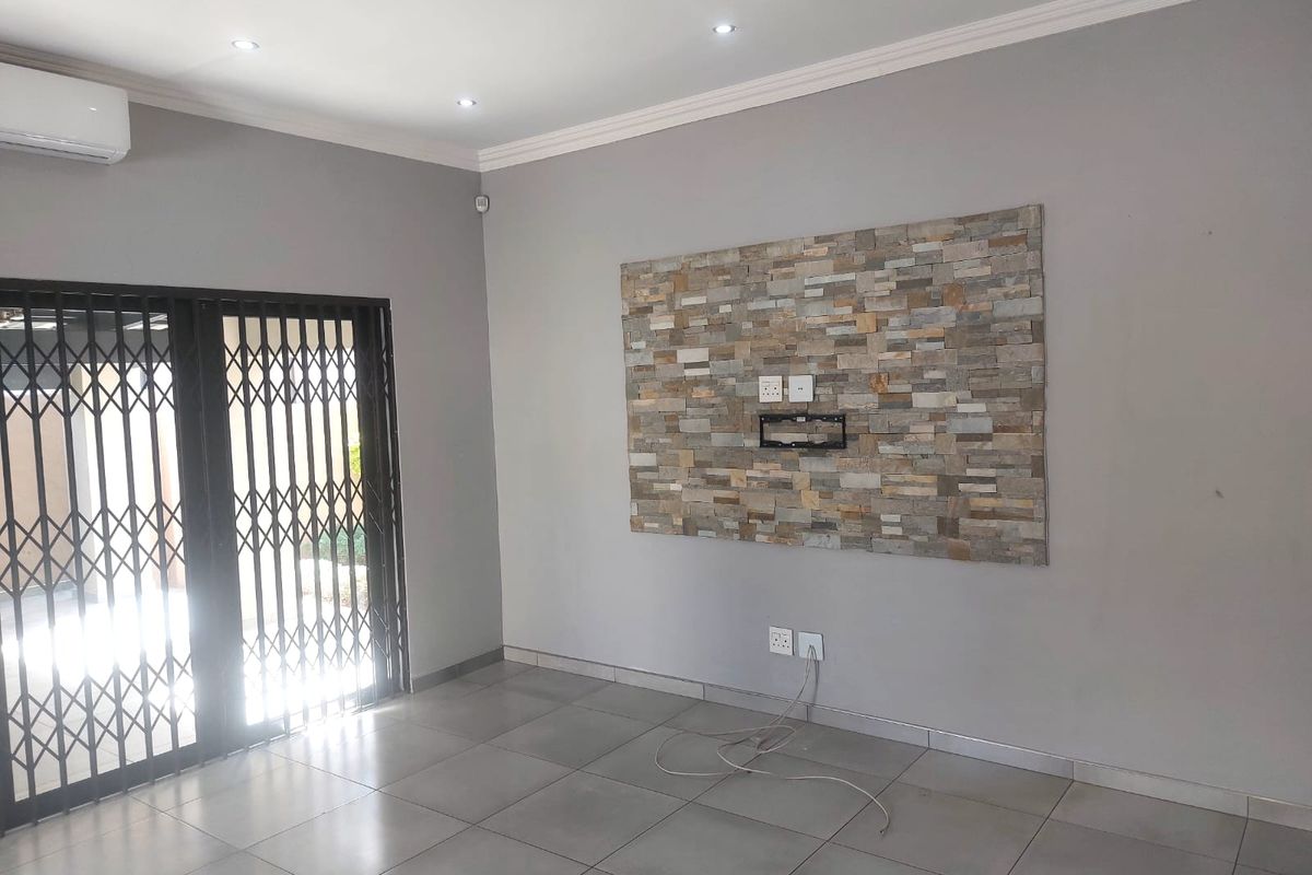 A bright, empty living room featuring a decorative stone feature wall, tiled flooring, recessed lighting, and a split-system air conditioner.
