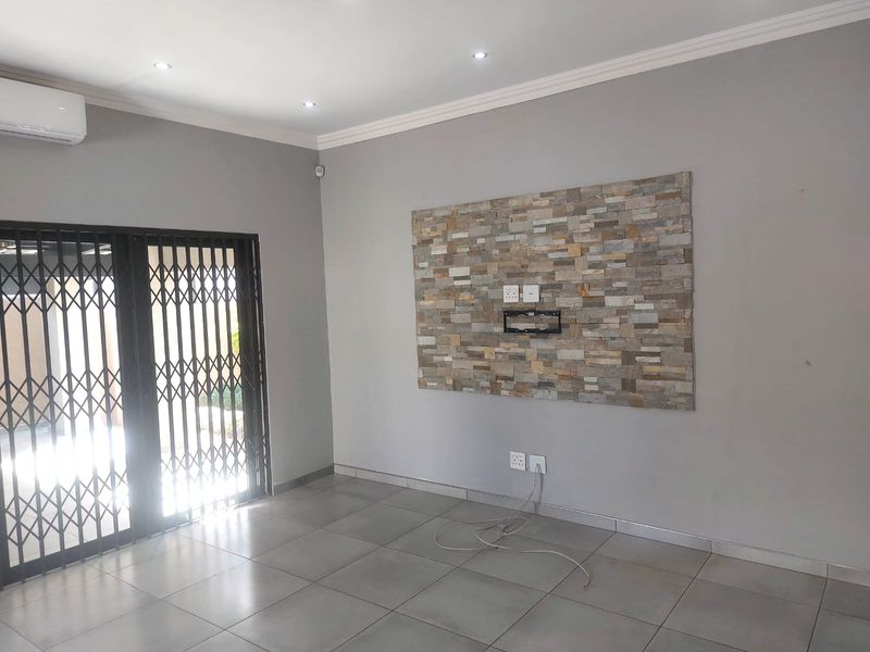 A bright, empty living room featuring a decorative stone feature wall, tiled flooring, recessed lighting, and a split-system air conditioner.