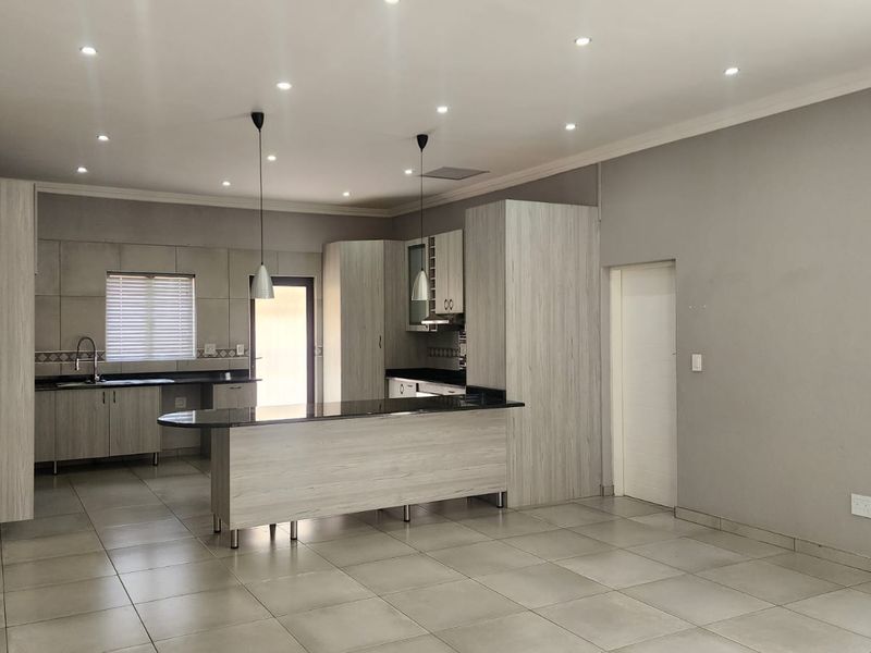 Spacious open-plan kitchen featuring modern light wood cabinetry, granite countertops, a central island, and neutral tiled flooring throughout.