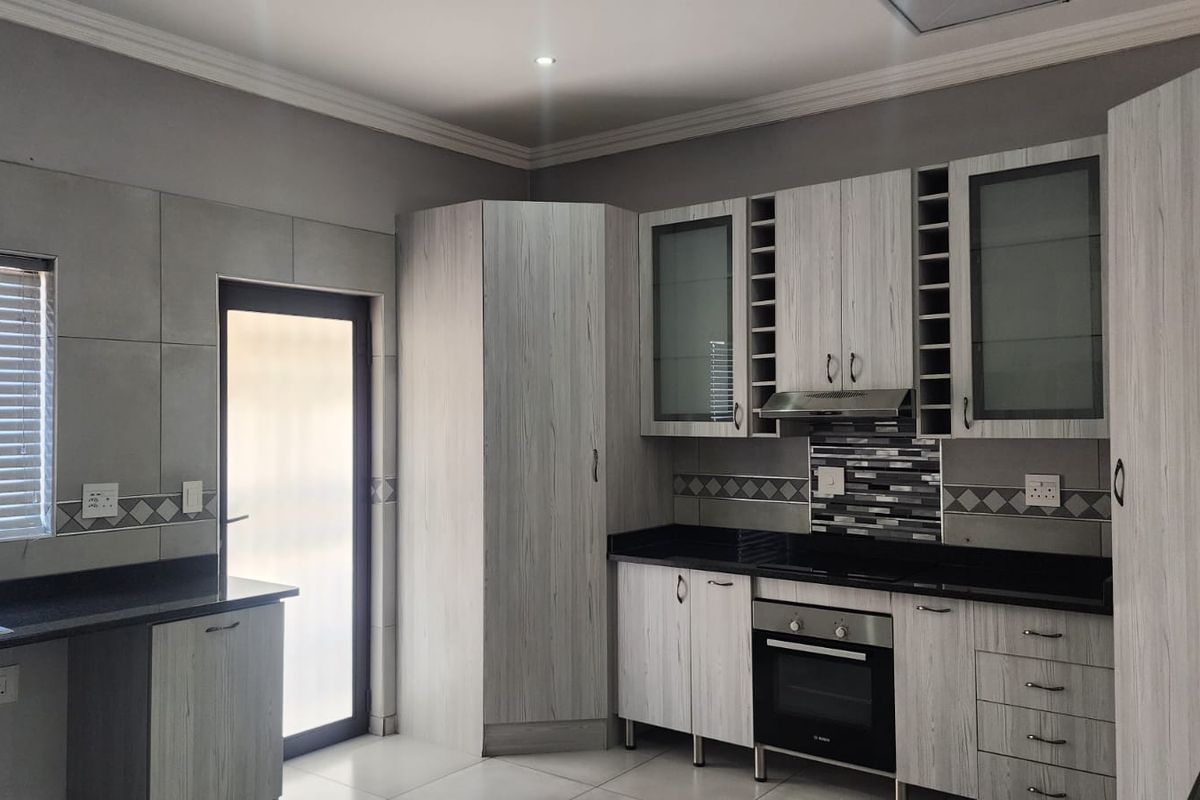 Modern kitchen featuring light wood-grain cabinetry, black granite countertops, built-in oven, extractor fan, and tiled backsplash with direct access to the exterior.