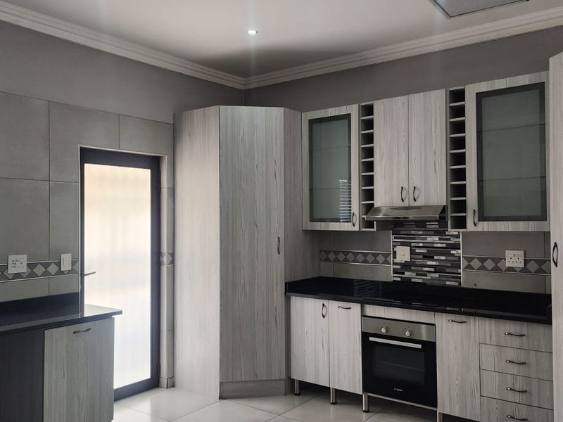Modern kitchen featuring light wood-grain cabinetry, black granite countertops, built-in oven, extractor fan, and tiled backsplash with direct access to the exterior.