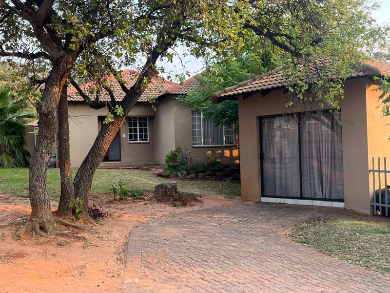 Front view of a single-story house featuring a tiled roof, paved driveway, and established garden with mature trees.