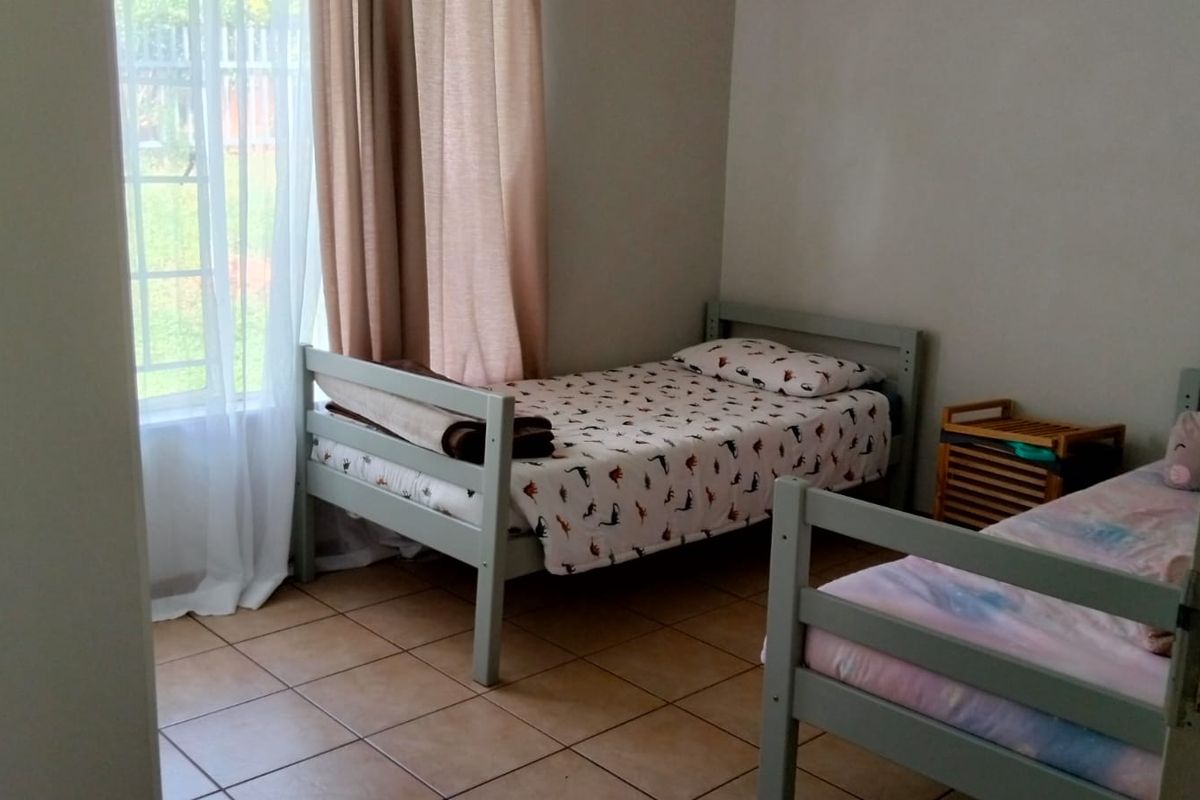 A functional bedroom featuring tiled flooring and a window with security bars, providing natural light and a practical layout.