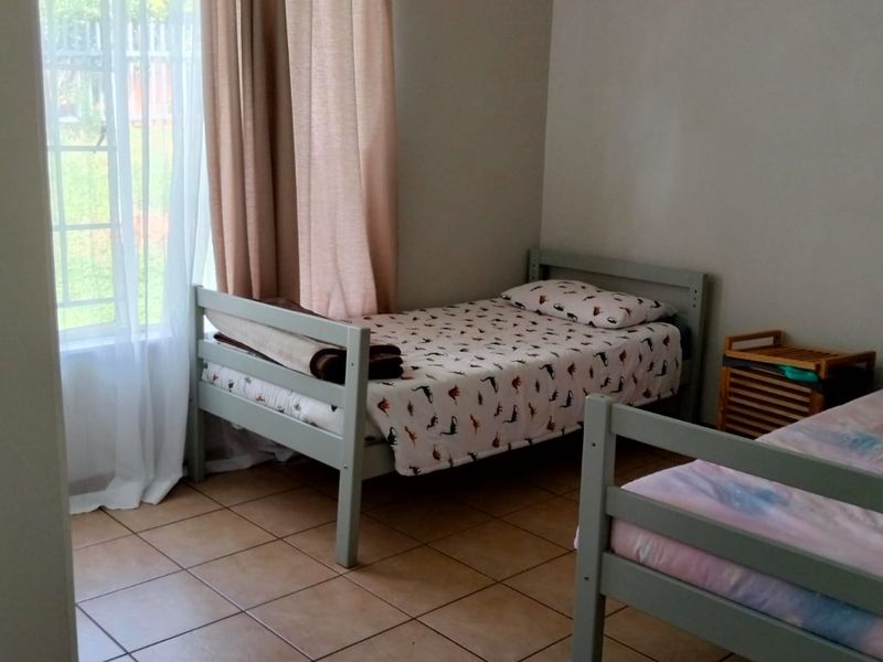 A functional bedroom featuring tiled flooring and a window with security bars, providing natural light and a practical layout.