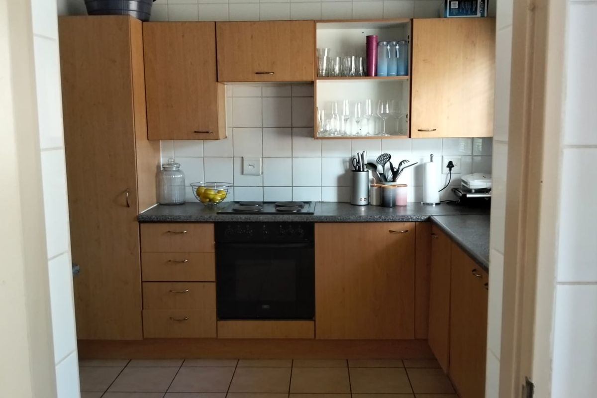 A functional kitchen featuring light wood-finish cabinetry, a built-in oven with electric hob, tiled backsplash, and durable ceramic floor tiles.