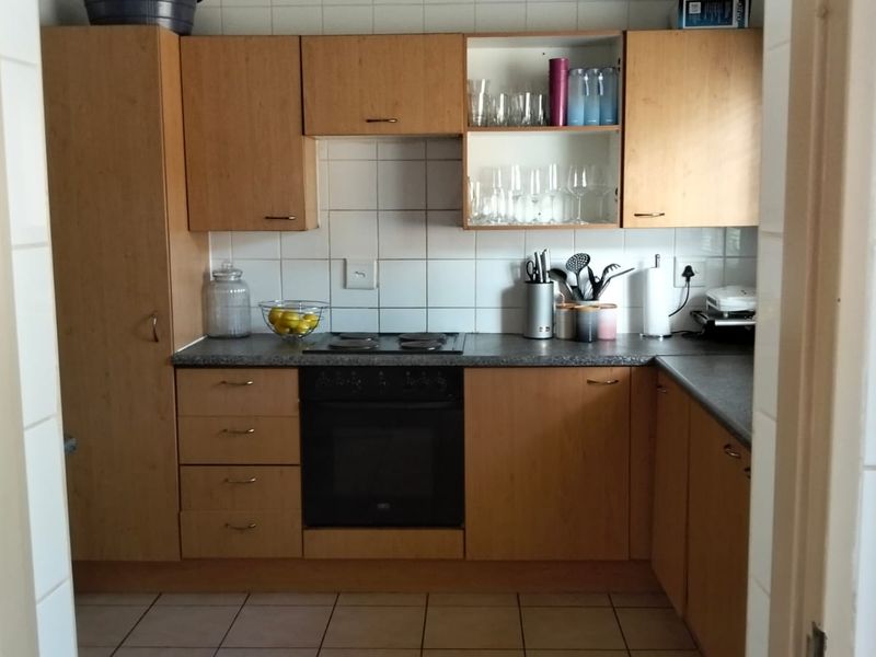 A functional kitchen featuring light wood-finish cabinetry, a built-in oven with electric hob, tiled backsplash, and durable ceramic floor tiles.