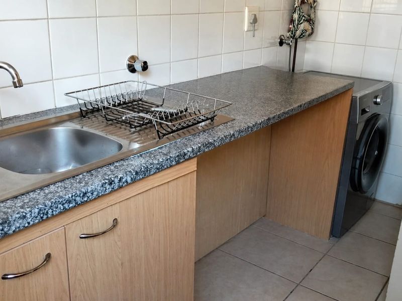 Functional laundry area featuring a stainless steel double sink, laminate countertops, tiled splashback, and built-in cabinetry with space for a washing machine.