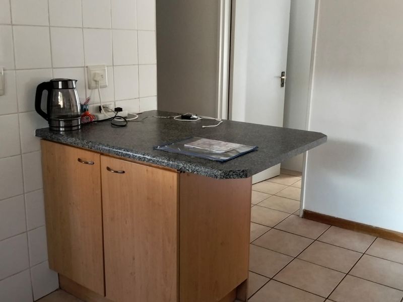 A compact kitchen area featuring laminate cabinetry, a stone-look countertop, and neutral ceramic tiling throughout.
