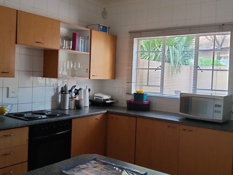 A functional kitchen featuring laminate cabinetry, dark countertops, an electric hob, and a tiled splashback, offering a practical layout with natural light.