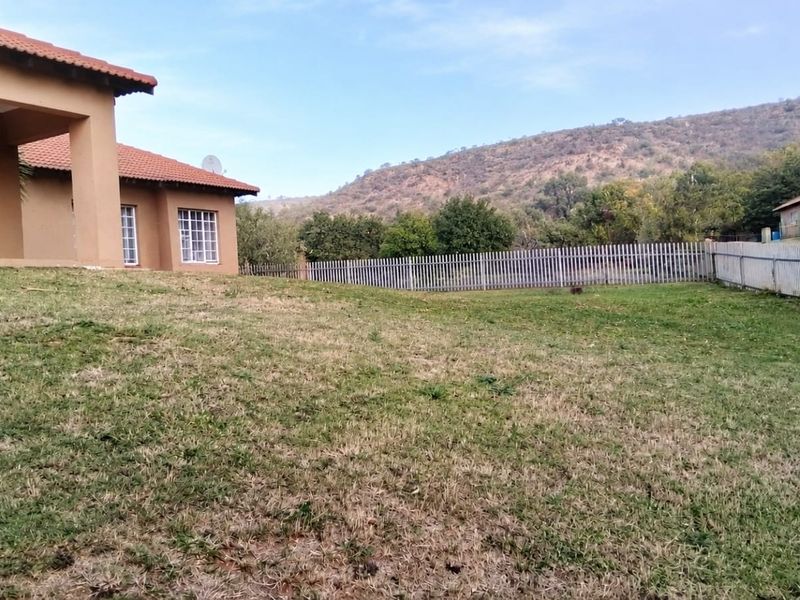 Spacious rear garden featuring a covered patio, terracotta roof tiles, and metal perimeter fencing with scenic mountain views.
