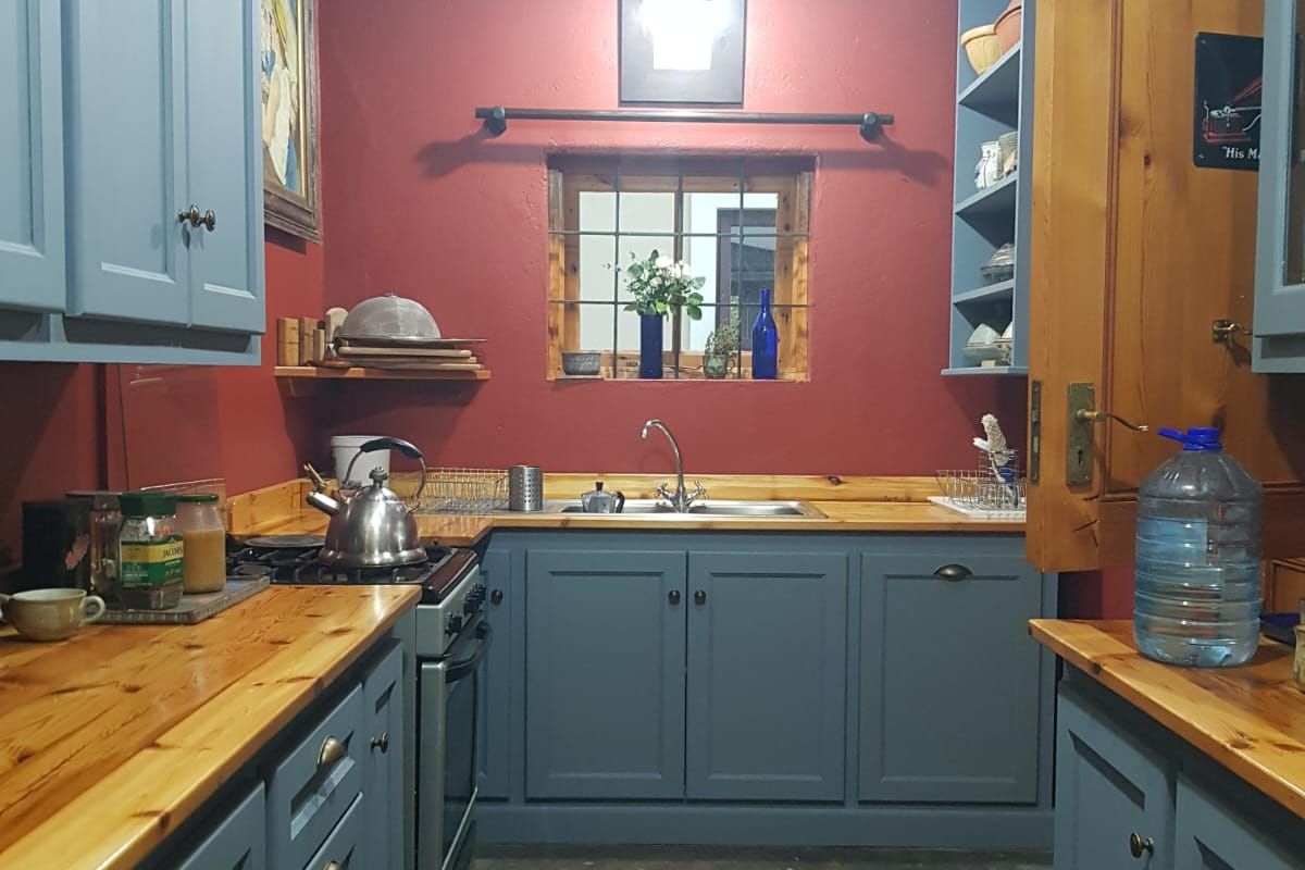 A compact kitchen featuring blue cabinetry, timber countertops, and a stainless steel sink, set against a bold red wall with a small window.