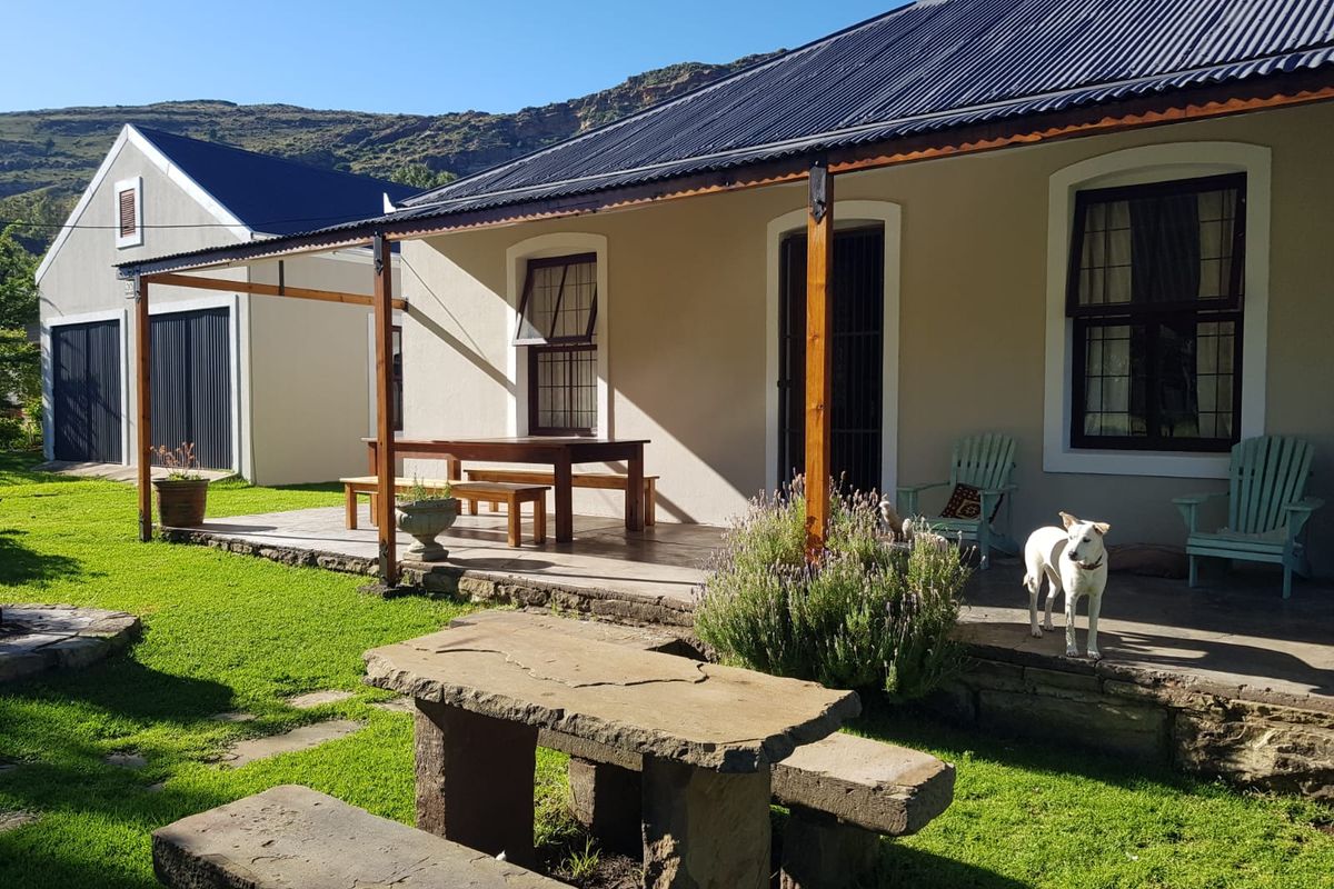 A well-maintained rear exterior view featuring a covered patio with timber posts, tiled flooring, and a stone garden bench set in a landscaped yard.