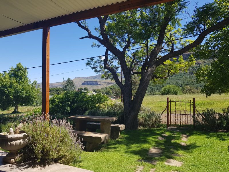 A covered patio area overlooking a lush garden with stone seating and scenic mountain views.