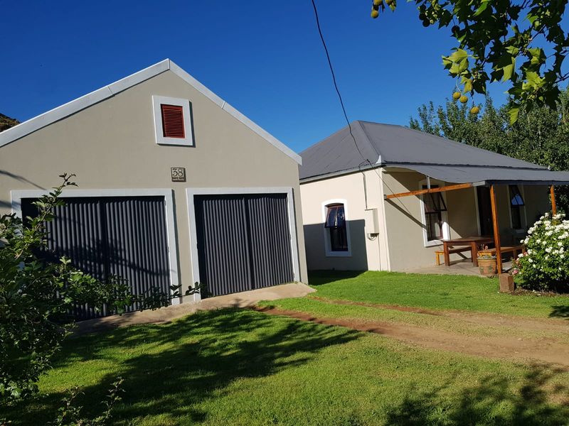 Front view of the property featuring a double garage with corrugated doors and a covered veranda area set within a well-maintained garden.