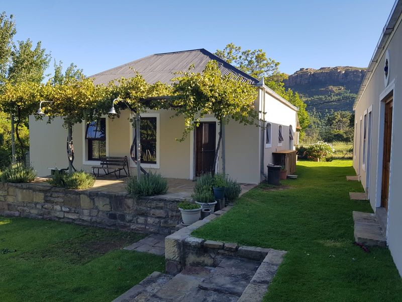 A well-maintained rear exterior view featuring a stone-paved patio with a pergola, stone retaining walls, and a lush garden setting with mountain views.