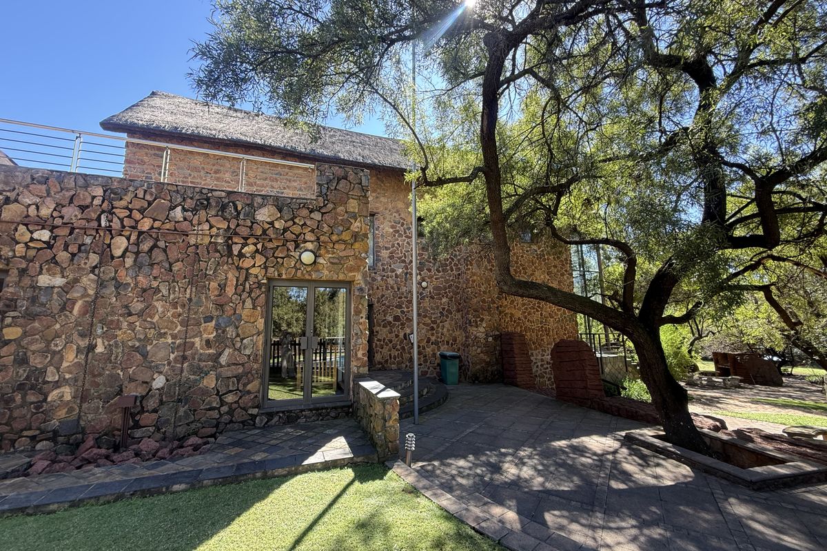 Rear view of a stone-clad residence featuring a thatched roof, paved patio area, and an upper-level balcony with metal railings.