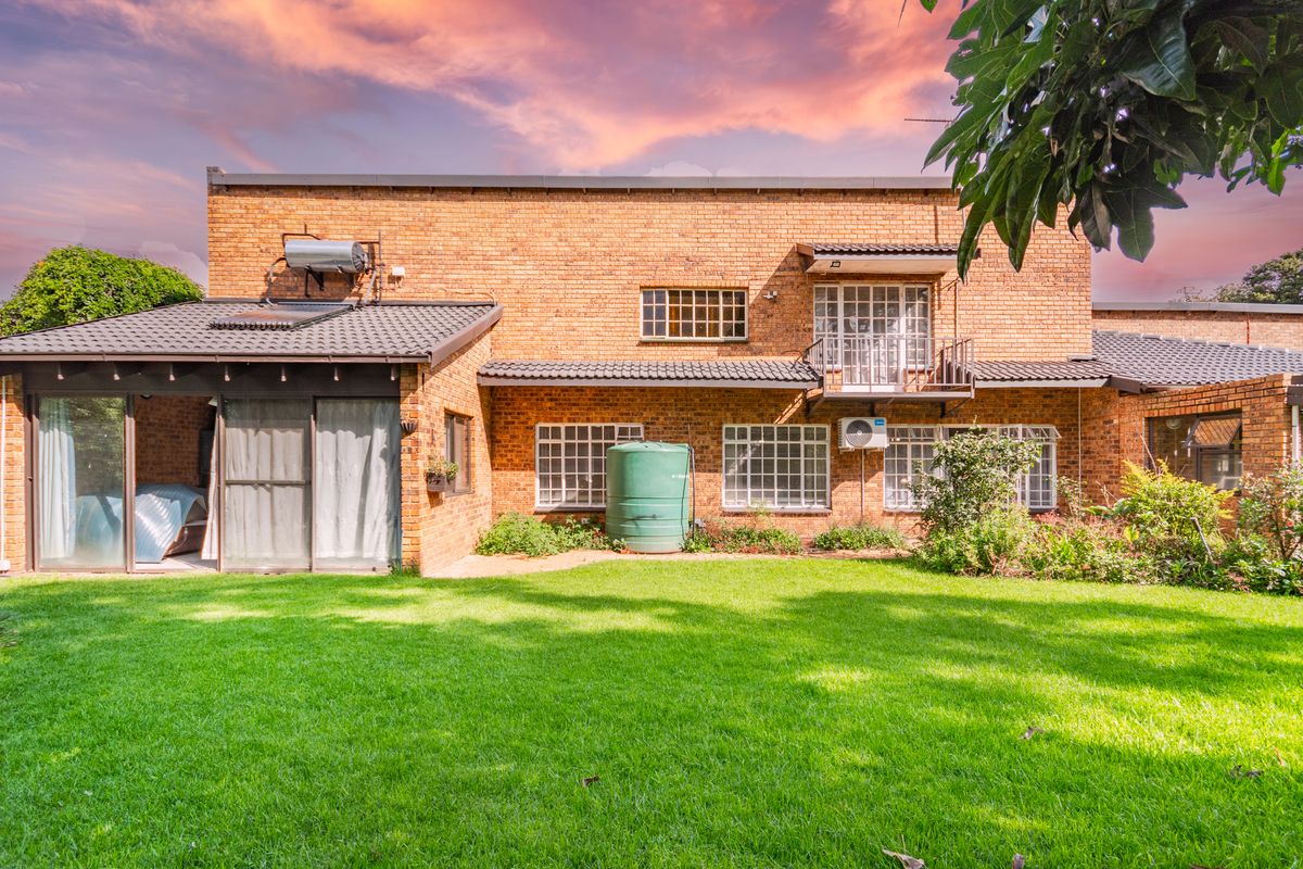 Rear view of a face brick house featuring a spacious lawn, solar water heating system, water storage tank, and a balcony.