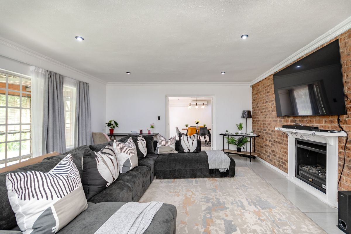 Spacious living room featuring an exposed brick feature wall, a built-in fireplace, and recessed downlighting, with a seamless flow to the adjacent dining area.