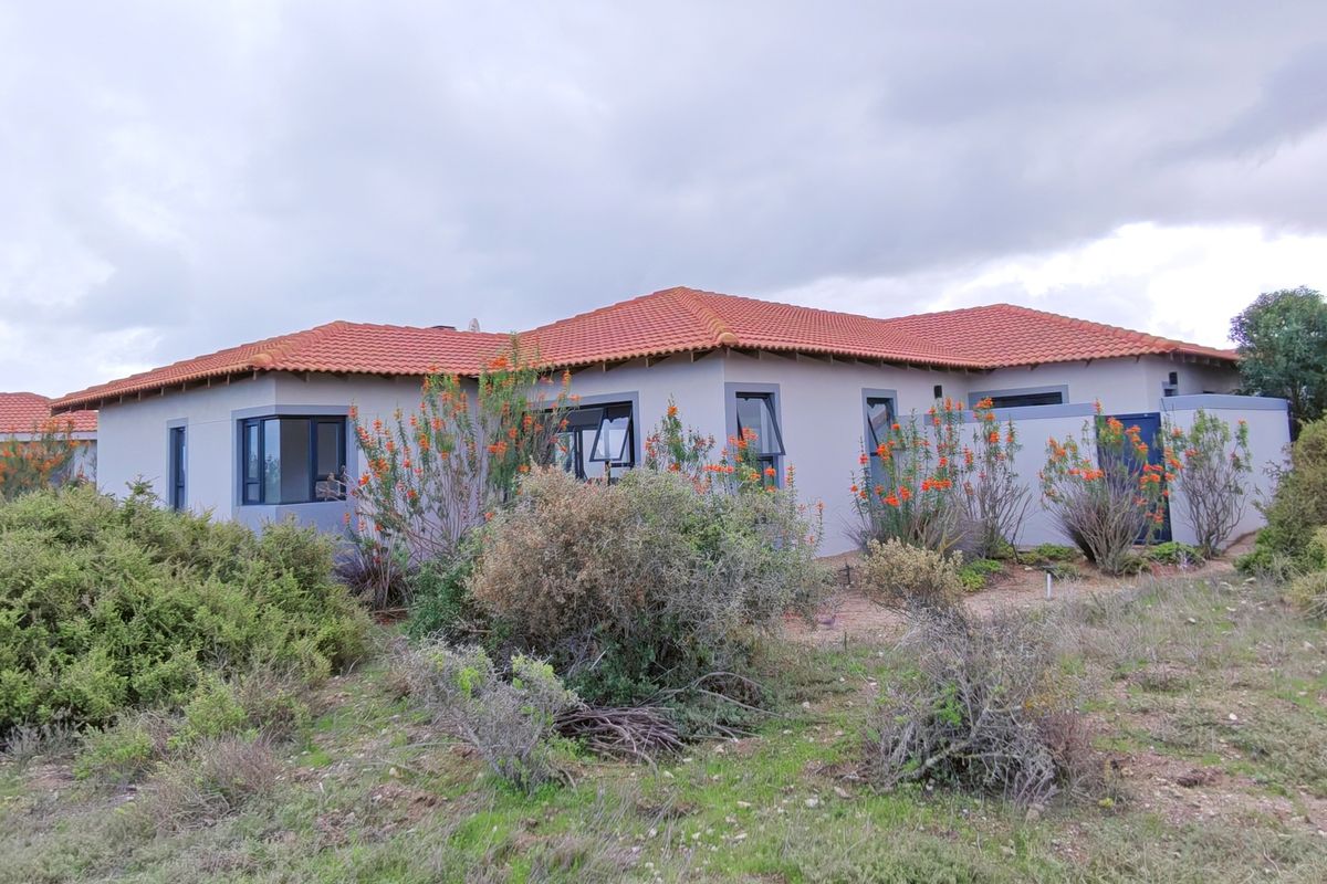 Rear view of a single-story residential house featuring terracotta roof tiles, plastered walls, and casement windows, set within a natural landscape.