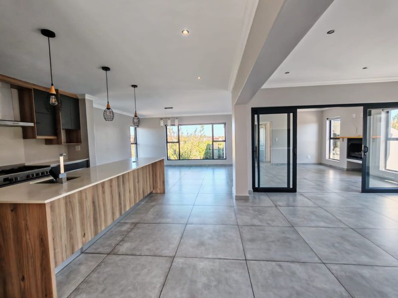 Spacious open-plan living area featuring a modern kitchen with stone island, tiled floors, and seamless flow to an adjacent room with a fireplace.