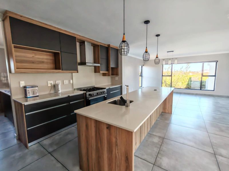Modern open-plan kitchen featuring a large island with stone countertops, sleek two-tone cabinetry, gas stove, and tiled flooring, flowing into a bright living area.