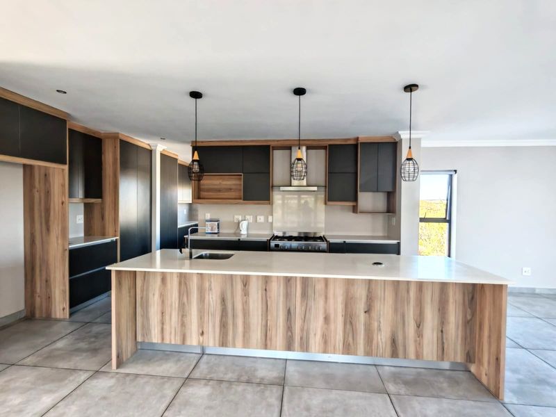 Modern kitchen featuring a large central island, dark cabinetry with wood-grain accents, stone countertops, and integrated gas stove with extractor fan.
