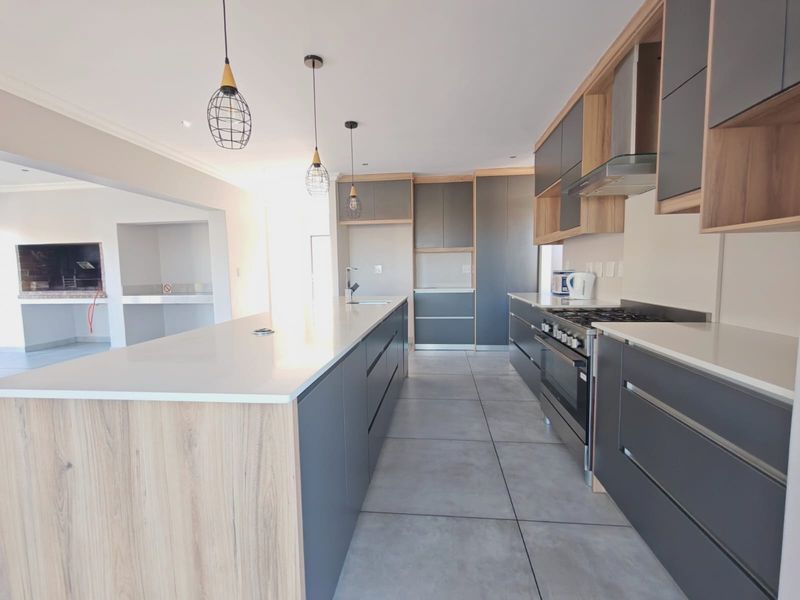 Modern kitchen featuring a large island with quartz countertops, sleek grey and wood-tone cabinetry, gas stove, and an adjacent built-in braai area.